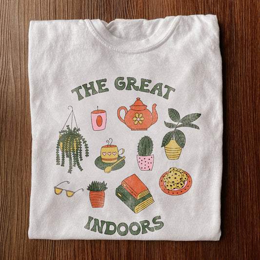 White shirt with the words The Great Indoors and drawings of indoor items like books, candles, and house plants